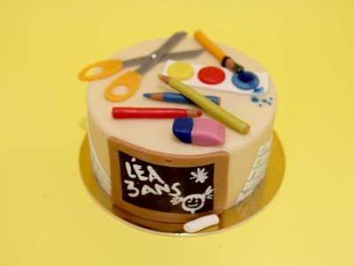 Gâteau d'anniversaire La maîtresse, avec des modelages représentant l'école : gomme, ciseau, stylo, crayon, gommettes...