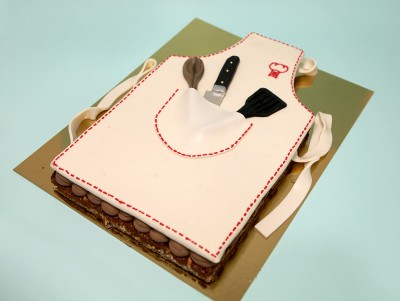 Gâteau Oui chef ! en forme de tablier de cuisine, avec des ustensiles, décoré à la main de la pâtisserie Chez Bogato.