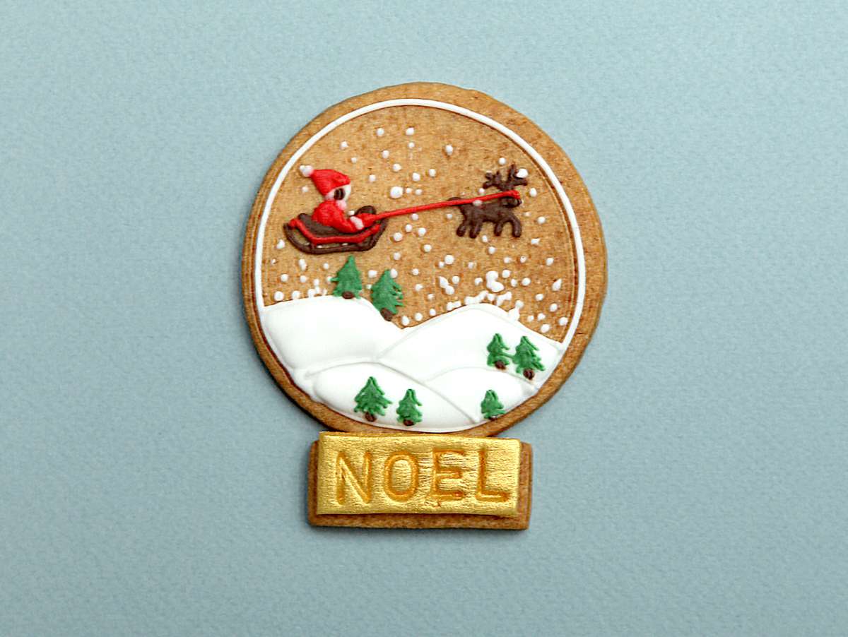 Sablé de Noël décoré à la main, avec le Père-Noël et son traineau s'envolant dans les airs dans un paysage enneigé.