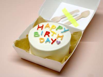 Bento cake Paris "Happy Birthday" de la pâtisserie Chez Bogato, au chocolat blanc et texte multicolore, à commander