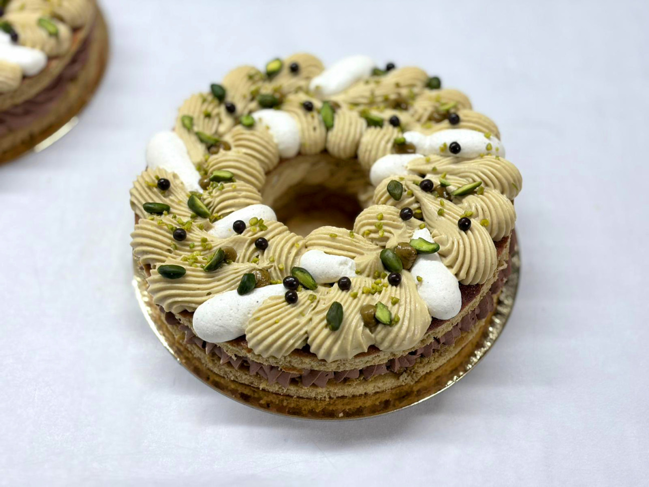 Tarte en forme de couronne avec croustillant pistache, praliné fondant pistache, ganache pistache et ganache chocolat.