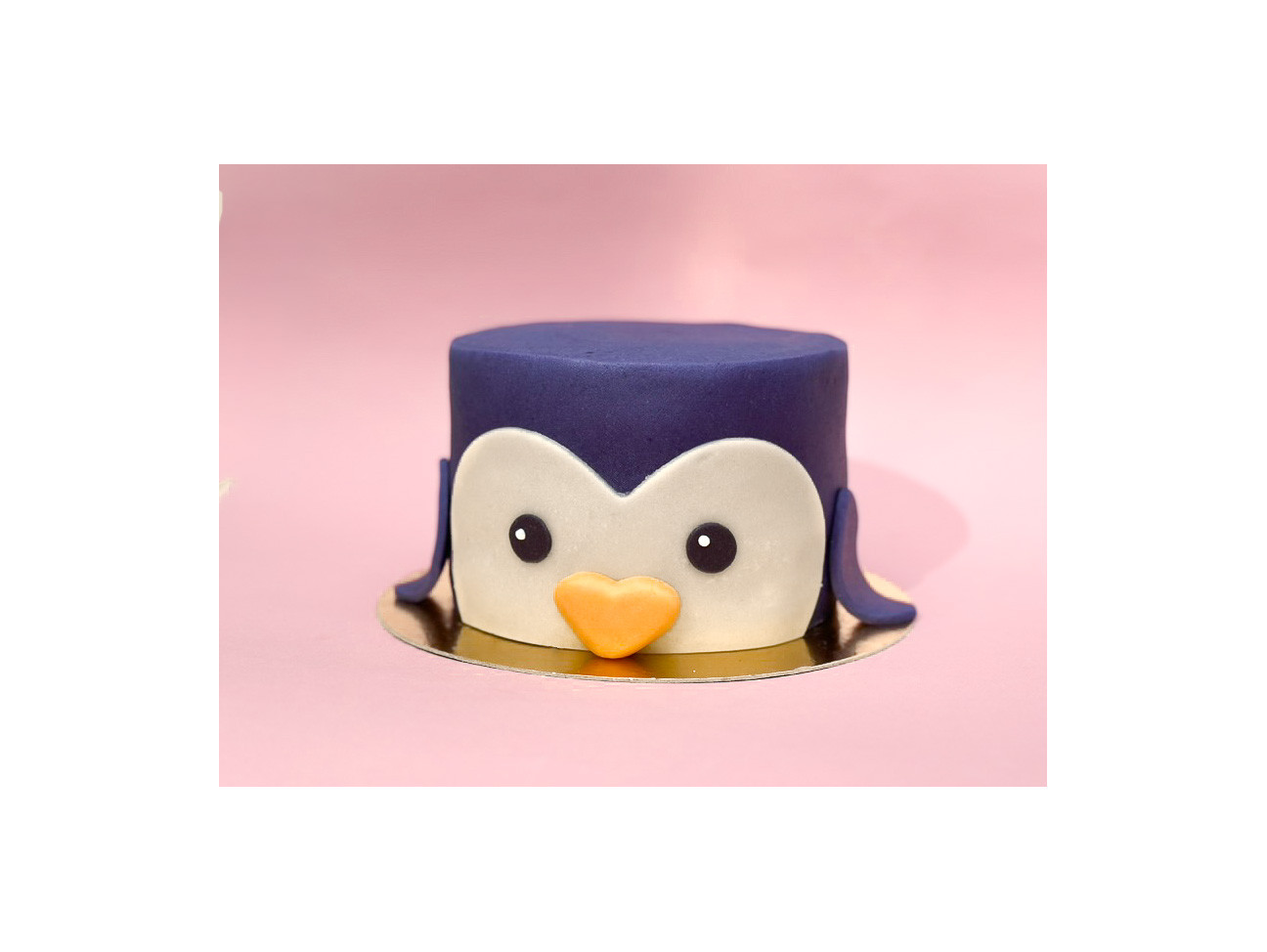 Gâteau décoré en forme de tête de pingouin bleu marine avec de grands yeux et un petit bec en pâte d'amande