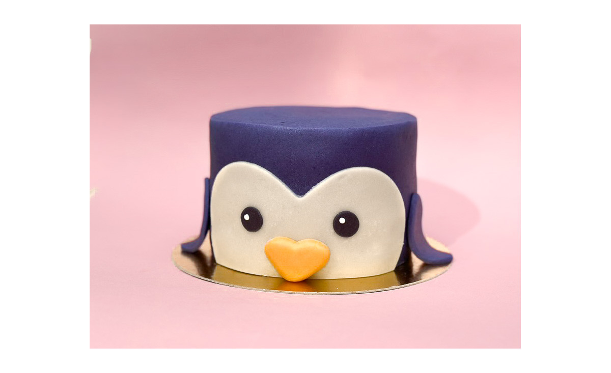 Gâteau décoré en forme de tête de pingouin bleu marine avec de grands yeux et un petit bec en pâte d'amande