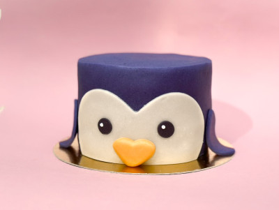 Gâteau décoré en forme de tête de pingouin bleu marine avec de grands yeux et un petit bec en pâte d'amande